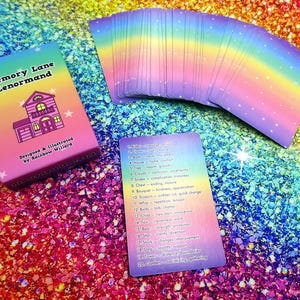 May include: A deck of "Memory Lane Lenormand" cards with a rainbow gradient design. The box features a house illustration and text. A spread of cards and a single card with numbered keywords are also visible, all on a glittery, rainbow-colored surface.