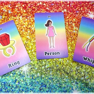 May include: Three colorful cards with illustrations and text. One card shows a ring with a large red gem and the word "Ring". Another card depicts a person in a pink dress with the word "Person". The third card shows a whip with the word "Whip".