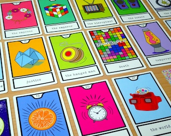 May include: A deck of tarot cards with colorful illustrations and white borders. Each card features a unique design, including a Rubik's Cube, a lava lamp, and a retro TV. The cards are arranged on a light brown surface.
