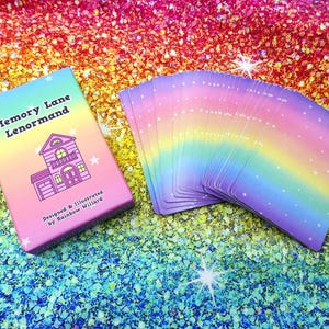 May include: A deck of Memory Lane Lenormand cards with a matching box. The box is pink and features a house illustration and the text "Memory Lane Lenormand". The cards have a rainbow gradient design with white stars.