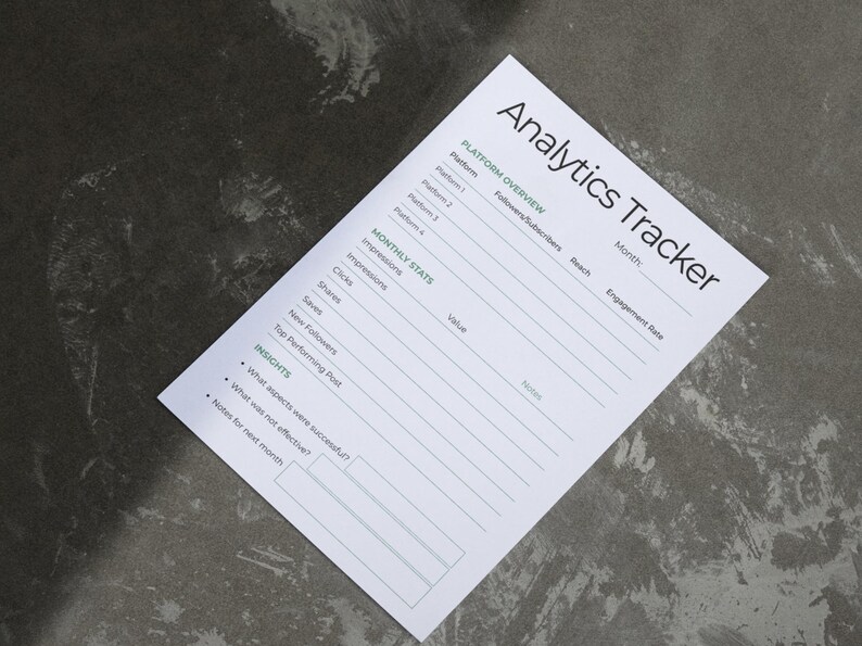 May include: A white paper titled "Analytics Tracker" on a gray surface. The paper includes sections for platform overview, monthly stats, and insights. The text is in black and green, with lines for filling in data. The paper is angled in the image.
