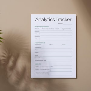May include: A white Analytics Tracker sheet with the title at the top. The sheet includes sections for platform overview, monthly stats, and insights. The sheet is on a beige surface with a plant shadow.