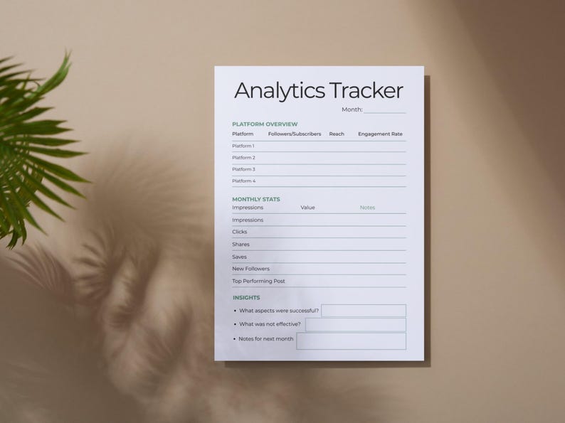 May include: A white Analytics Tracker sheet with the title at the top. The sheet includes sections for platform overview, monthly stats, and insights. The sheet is on a beige surface with a plant shadow.