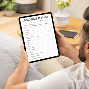 May include: A black tablet displaying an "Analytics Tracker" form. The form includes sections for platform overview, monthly stats, and insights. The tablet is held by a person sitting on a couch.