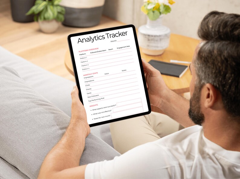 May include: A black tablet displaying an "Analytics Tracker" form. The form includes sections for platform overview, monthly stats, and insights. The tablet is held by a person sitting on a couch.