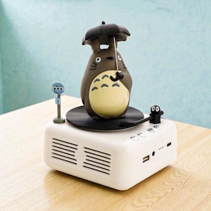 Pu&ograve; includere: Un altoparlante bianco con una statuetta di Totoro che tiene un ombrello. L'altoparlante ha una base per giradischi nera, un piccolo microfono e una piccola figura nera. Include una porta USB e un ingresso di linea.