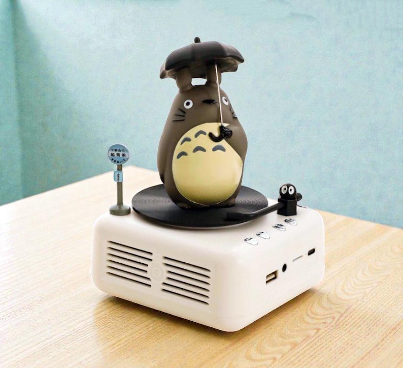 Pu&ograve; includere: Un altoparlante bianco con una statuetta di Totoro che tiene un ombrello. L'altoparlante ha una base per giradischi nera, un piccolo microfono e una piccola figura nera. Include una porta USB e un ingresso di linea.