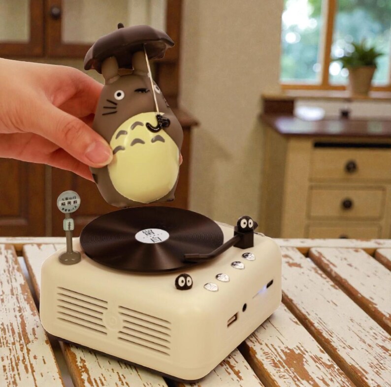 Pu&ograve; includere: Un giradischi retr&ograve; color crema con un disco in vinile marrone. Un personaggio dei cartoni animati marrone e beige con un ombrello &egrave; tenuto sopra il giradischi. Il giradischi ha un altoparlante e diversi pulsanti.