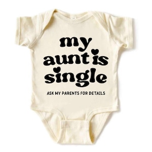 May include: A cream-colored short-sleeve baby bodysuit featuring black text that reads "my aunt is single" with two small heart icons, followed by the text "ASK MY PARENTS FOR DETAILS" in a smaller, sans-serif font centered on the chest.