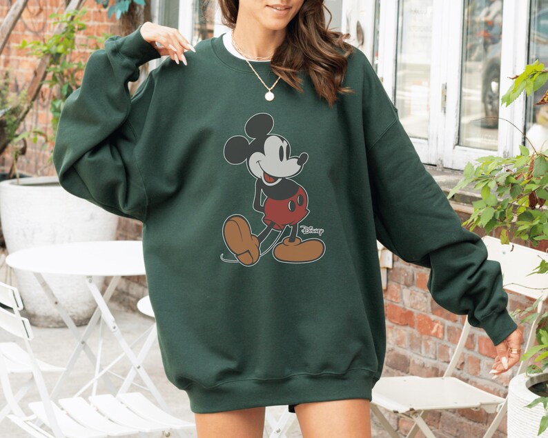 May include: Dark green sweatshirt featuring a classic Mickey Mouse graphic. The cartoon character is depicted in black, red, and tan colors. The sweatshirt has long sleeves and a crew neck.