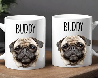 May include: Two white ceramic mugs with the word "BUDDY" printed in black above a pug's face. The pug has a tan coat, black ears, and a black muzzle. The mugs are on a wooden tray.