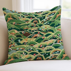 May include: Square throw pillow with a repeating pattern of rolling green hills. The design includes stylized deer, flowers, and foliage in shades of green, brown, and red. The pillow is on a white sofa.