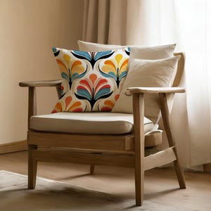 May include: A wooden armchair with a beige cushion and pillows. A decorative pillow with a colorful floral pattern in orange, yellow, blue, and black sits on the chair. The chair is in front of a beige curtain.