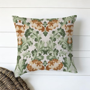 Puede incluir: Cojín cuadrado con un estampado floral. El diseño presenta grandes flores estilizadas en tonos marrón y crema, sobre un fondo claro. El follaje y las hojas verdes llenan los espacios entre las flores. El cojín es probablemente de tela.