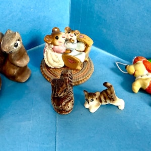 May include: A collection of six small animal figurines including two brown squirrels, a pair of mice in a cradle on a woven base, a small brown textured animal, a white and brown striped kitten, and a yellow and orange dog with a white string.