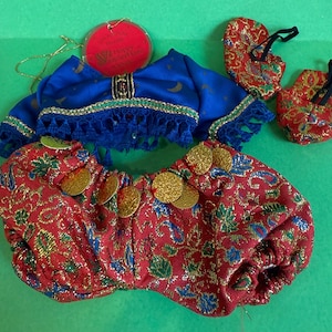 May include: A miniature belly dance costume set. The set includes a blue top with gold trim and fringe, red patterned bottoms with gold coins, and two red patterned shoes. The costume is designed with a Middle Eastern theme.