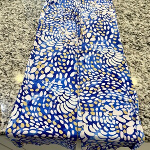 May include: Wide-leg pants with a blue, white, and gold abstract print. The print features a swirling pattern of dots and lines.