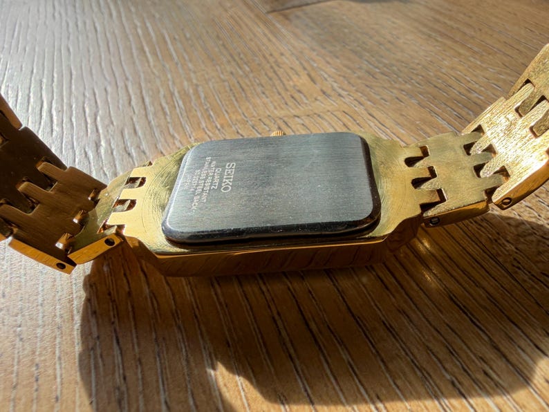 Pu&ograve; includere: Un orologio da polso color oro con cassa rettangolare e bracciale a maglie abbinato. Il retro della cassa &egrave; in acciaio inossidabile color argento e riporta la scritta SEIKO, QUARTZ, WATER RESISTANT, STAINLESS STEEL BACK e JAPAN.