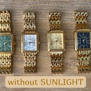 Pu&ograve; includere: Quattro orologi da polso rettangolari Seiko con cinturini a maglie color oro. Gli orologi presentano quadranti verde, bianco, oro e nero, ciascuno con numeri romani e lancette dorate. Il testo without SUNLIGHT &egrave; visibile.