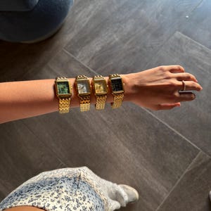 Pu&ograve; includere: Quattro orologi da polso rettangolari con cinturini a maglie in metallo dorato disposti in fila su un braccio. Gli orologi presentano quadranti di diversi colori, tra cui verde, bianco, oro e nero, ciascuno in una cassa dorata coordinata.