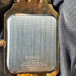 Pu&ograve; includere: Un orologio color oro con cassa rettangolare e fondello in acciaio inossidabile spazzolato. Il retro &egrave; inciso con SEIKO, QUARTZ, WATER RESISTANT, STAINLESS STEEL BACK, 50 325714 e JAPAN. L'orologio presenta un cinturino a maglie in metallo dorato.
