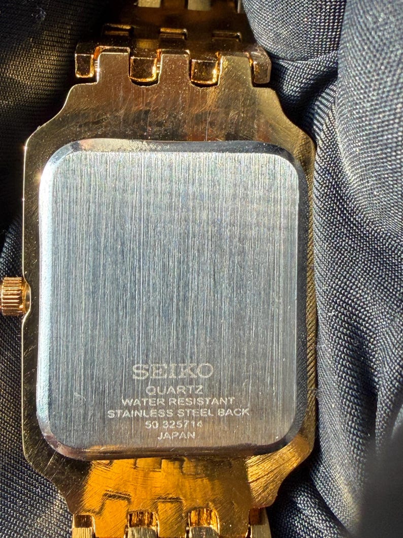 Pu&ograve; includere: Un orologio color oro con cassa rettangolare e fondello in acciaio inossidabile spazzolato. Il retro &egrave; inciso con SEIKO, QUARTZ, WATER RESISTANT, STAINLESS STEEL BACK, 50 325714 e JAPAN. L'orologio presenta un cinturino a maglie in metallo dorato.