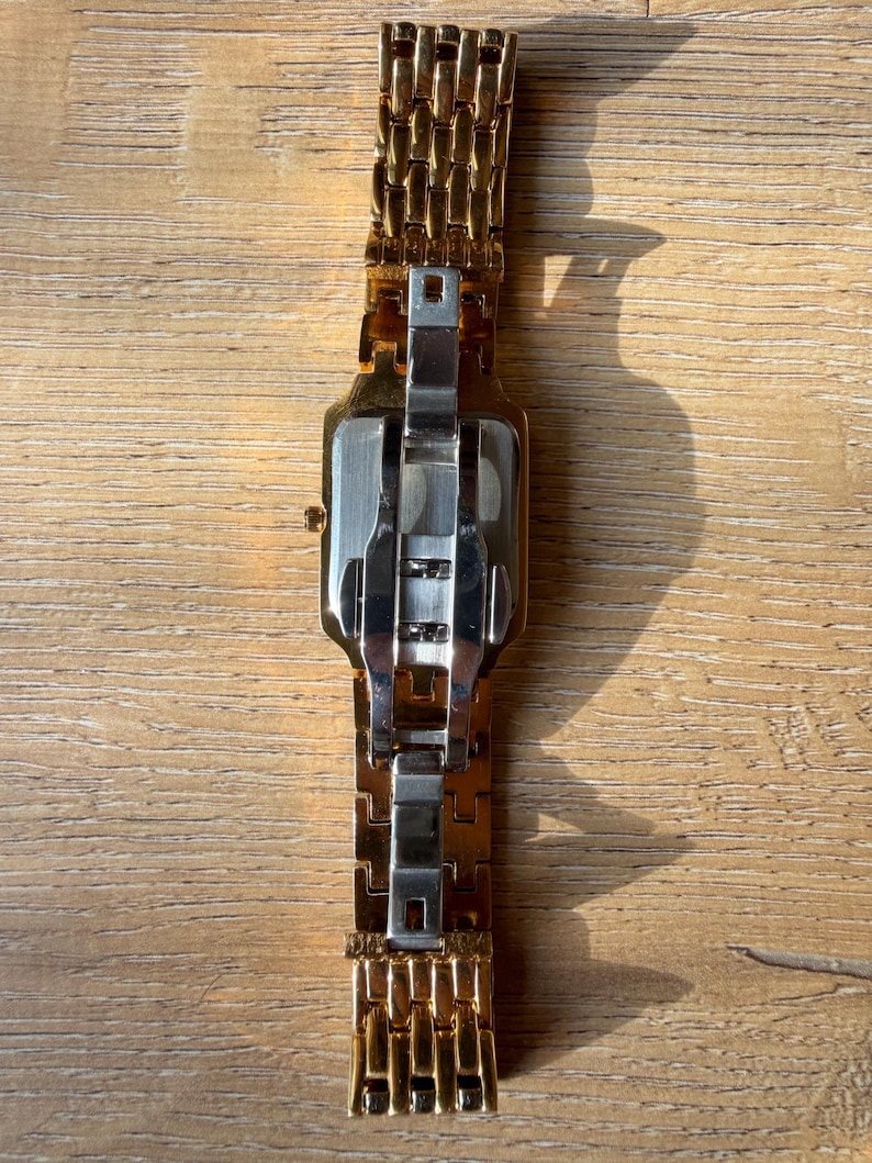 Pu&ograve; includere: Un orologio da polso in metallo color oro con cassa rettangolare e bracciale a maglie multiple. Il retro della cassa &egrave; color argento e il bracciale include una chiusura a farfalla in acciaio inossidabile color argento.