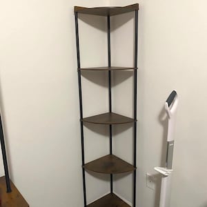 May include: A corner shelf unit with five triangular shelves. The shelves are a dark brown color, and the frame is black. The unit is made of metal and wood. The shelves are supported by vertical black metal poles.
