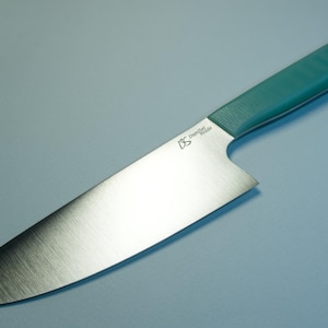 Peut inclure: Un couteau de chef en acier inoxydable avec un manche turquoise. La lame est argentée et légèrement incurvée. Le manche est de couleur turquoise unie. Le couteau porte l'inscription "Diamond Blade" sur la lame.