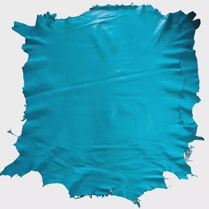 May include: A large piece of turquoise leather with an irregular shape. The leather has a smooth, slightly glossy finish and a jagged edge. The colour is a vibrant turquoise, with slight variations in tone across the surface.