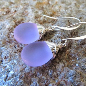 May include: A pair of silver dangle earrings with lavender glass teardrop beads wrapped in silver wire.