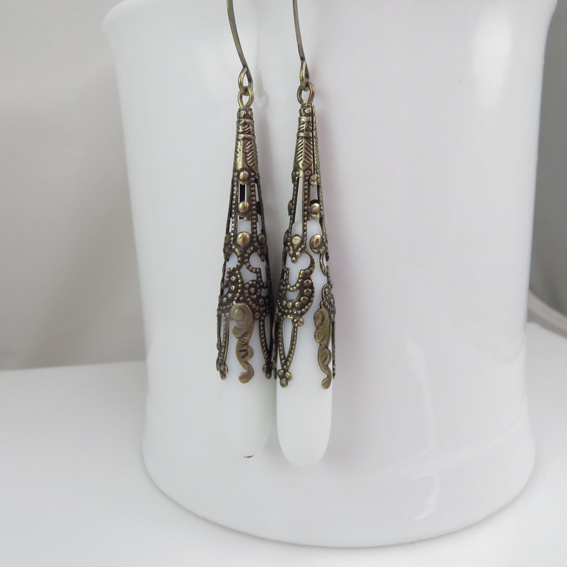 May include: A pair of white teardrop-shaped earrings with intricate gold filigree designs.