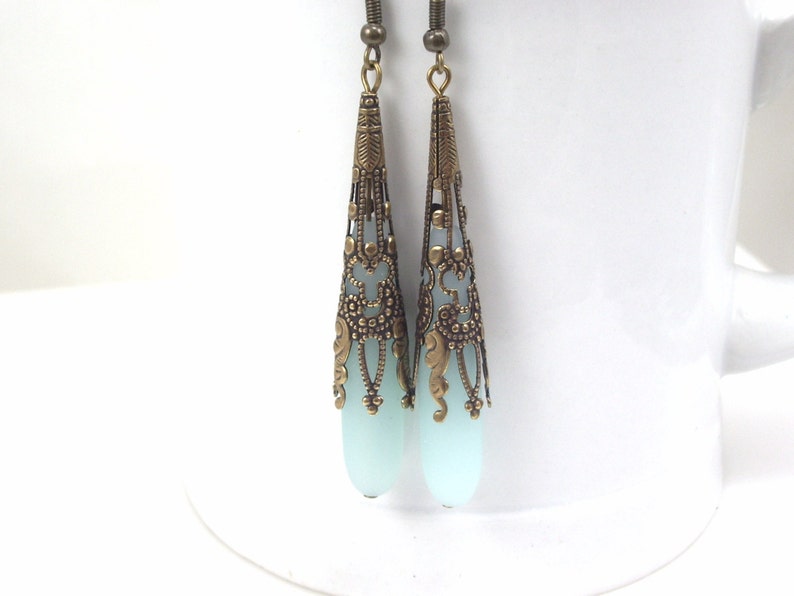May include: A pair of dangle earrings with a light blue glass teardrop shape and a gold filigree design.