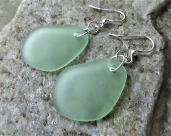 May include: A pair of earrings with light green sea glass stones and silver hooks.