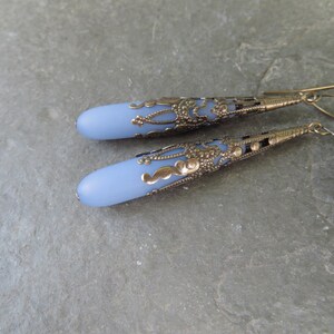 May include: A pair of dangle earrings with a light blue glass teardrop shape and a detailed silver filigree design.