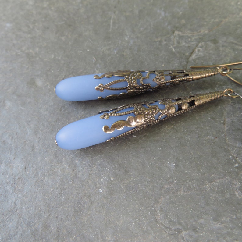 May include: A pair of dangle earrings with a light blue glass teardrop shape and a detailed silver filigree design.