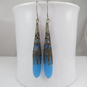 May include: A pair of dangle earrings with a blue glass teardrop shape and a gold filigree design.