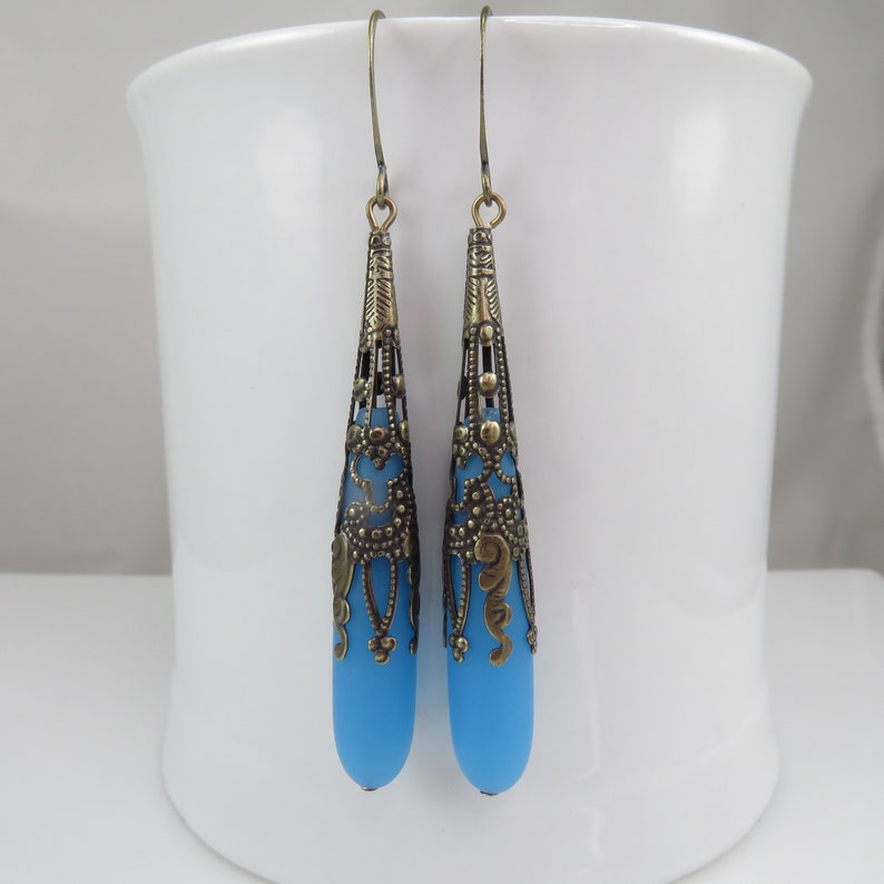 May include: A pair of dangle earrings with a blue glass teardrop shape and a gold filigree design.