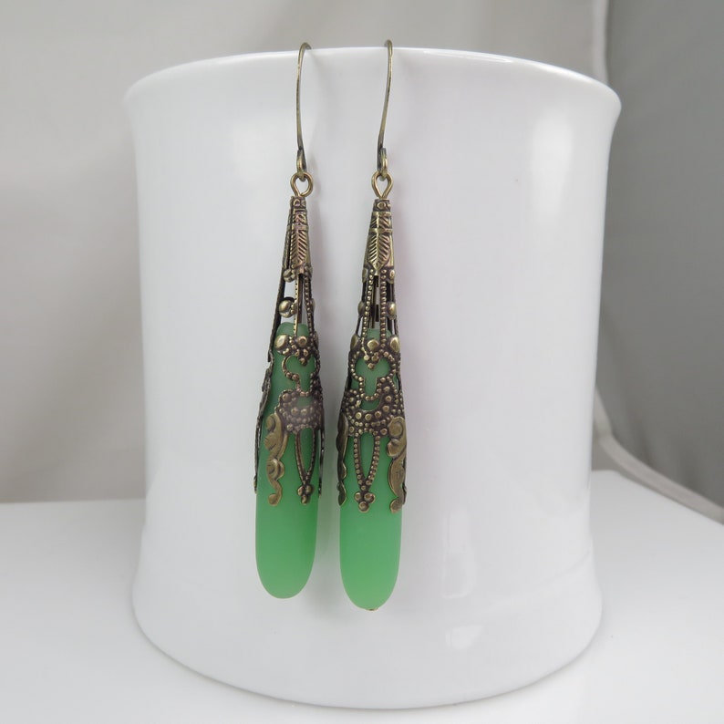 May include: A pair of dangle earrings with green glass beads and ornate brass filigree.