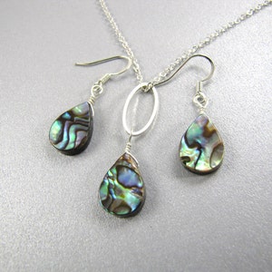 May include: A silver necklace with a teardrop-shaped abalone shell pendant and matching earrings. The necklace has a simple chain and a circular pendant.