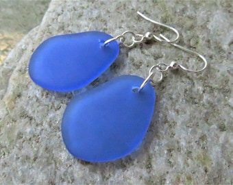 May include: A pair of earrings featuring blue sea glass stones with silver hooks.