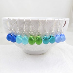 May include: Eight pairs of teardrop-shaped glass earrings in shades of blue and green, hanging from silver hooks.