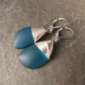 May include: Teal blue glass earrings with silver wire wrapped around the edges. The earrings have silver hooks.