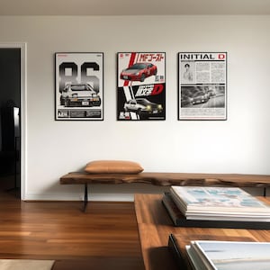 May include: Three framed posters featuring Japanese car designs. The posters showcase the Toyota AE86, GT 86, and Initial D. The posters are black and white with red accents, and are displayed on a white wall above a wooden bench.