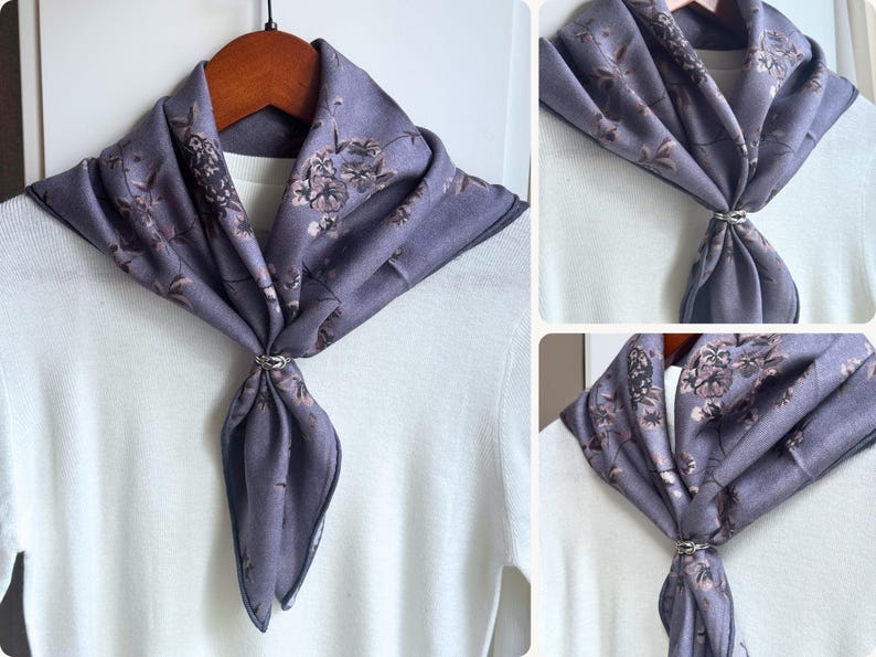 May include: A lavender scarf with a floral pattern, secured with a silver-colored ring. The scarf is draped over a white top, creating a stylish accessory. The scarf is made of a soft material.