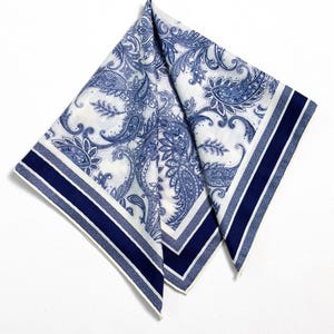 May include: White and blue paisley patterned handkerchief. The handkerchief features a detailed floral design in shades of blue against a white background. The edges are trimmed with a navy blue stripe and a thin white stripe.