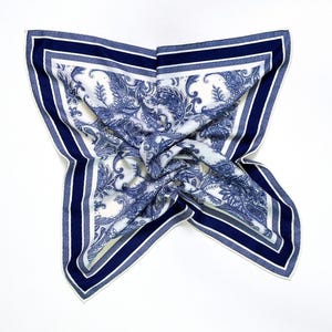May include: A square scarf with a white background and a blue paisley pattern. The scarf has a navy blue border with a white stripe. The text "30% Mulberry Silk + 70% Wool" is at the bottom.