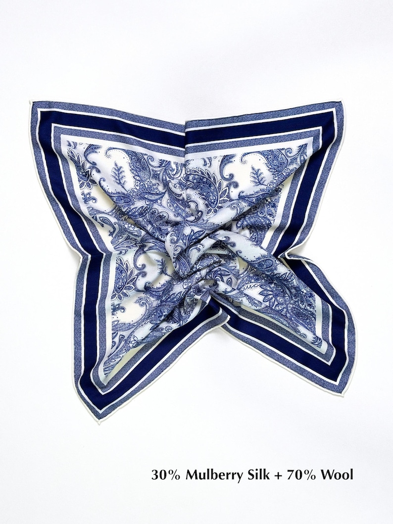 May include: A square scarf with a white background and a blue paisley pattern. The scarf has a navy blue border with a white stripe. The text "30% Mulberry Silk + 70% Wool" is at the bottom.