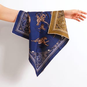 May include: A square scarf featuring a deep blue central panel with a repeating pattern of leaping cheetahs. The scarf is bordered by intricate paisley designs in shades of dark blue, white, and a contrasting olive green corner section.