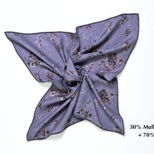 May include: A lavender scarf with a floral pattern in shades of brown and gray. The scarf is made of 30% mulberry silk and 70% wool. The edges are finished with a dark gray border. The scarf is displayed on a white background.